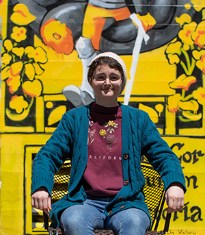 Emma Wakefield sits in a chair in front of a mural she created at the Sculpture Yard on campus