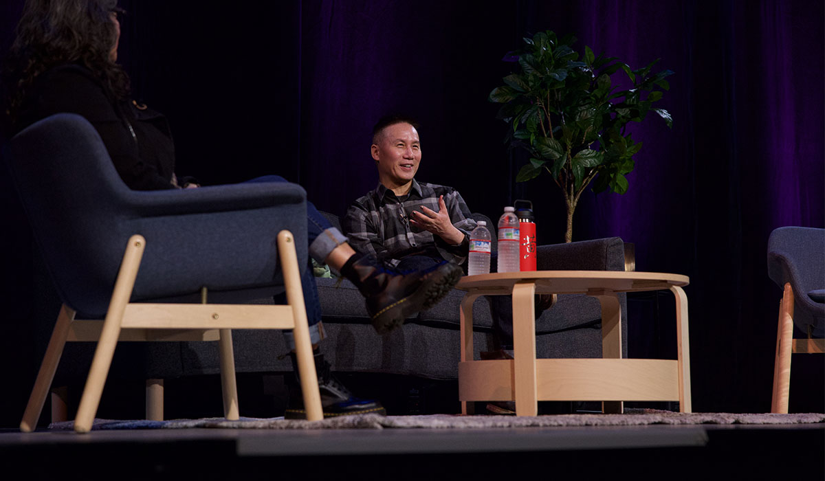 Actor BD Wong sits in a chair on a stage across from a woman