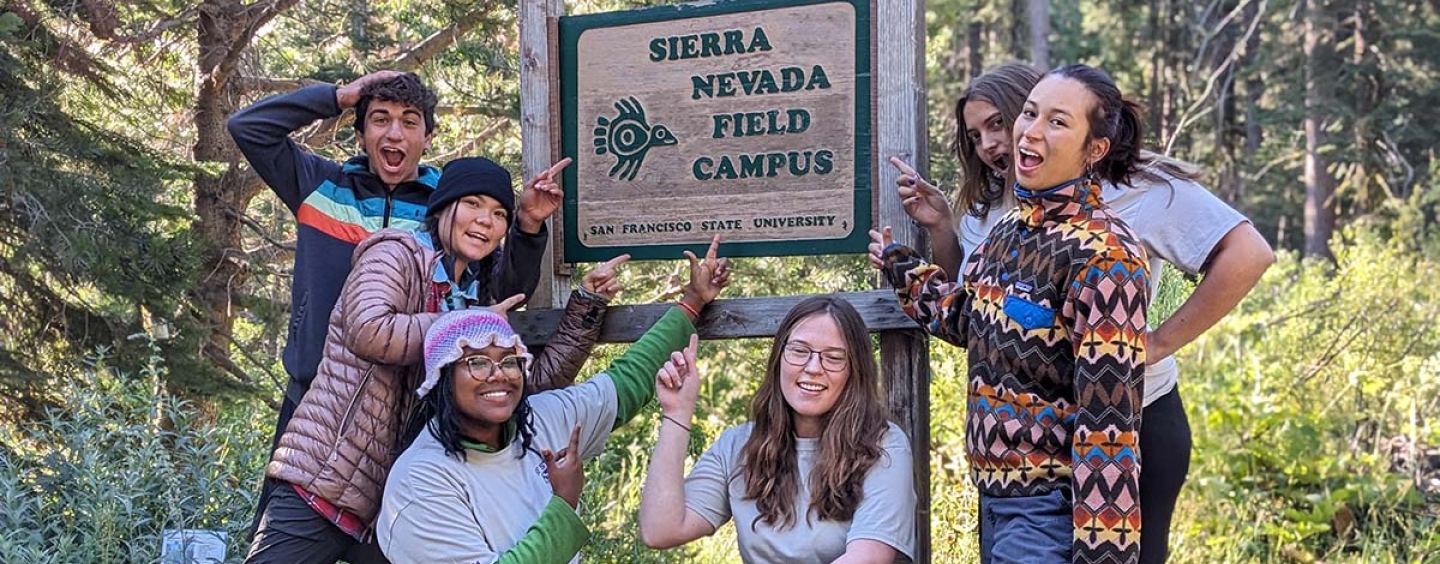 Six students smiling and pointing to the Sierra Nevada Field Campus Sign