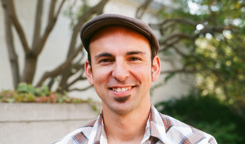 Federico Ardila, wearing a cap and plaid shirt, looks directly at the camera