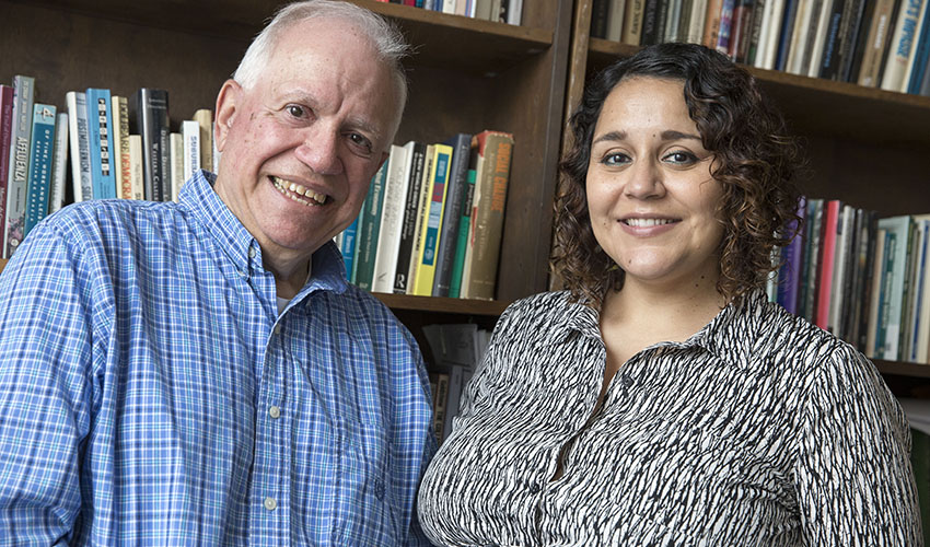 Professors Joel Kassiola and Marcela Garcia-Castañon are smiling with book-lined shelves in the background.