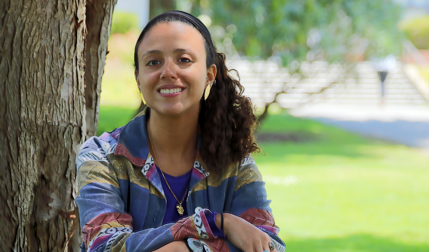 Graduate student Salma Abdel-Raheem looks at the camera with campus greenery in the background