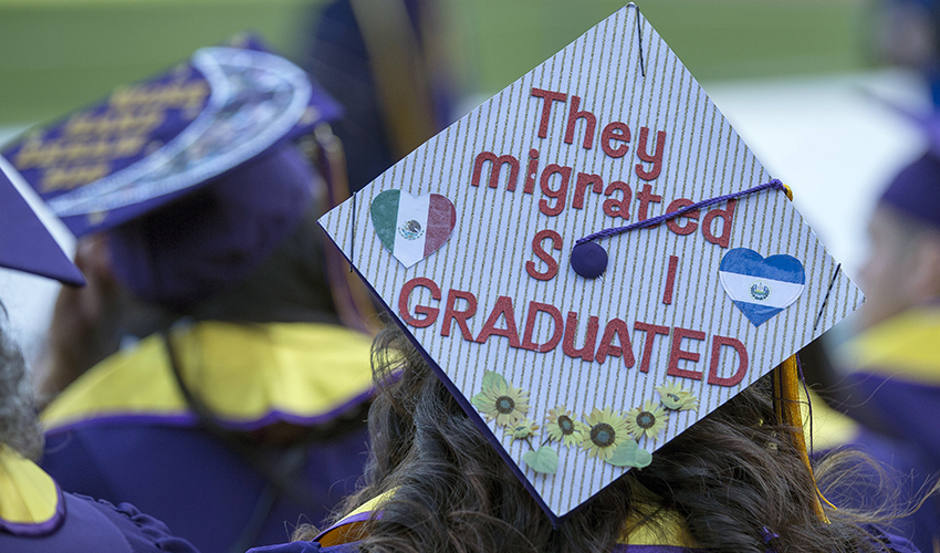 A graduate’s mortarboard features pinstripes, heart-shaped flags of Mexico and El Salvador, images of flowers and the statement They migrated so I graduated