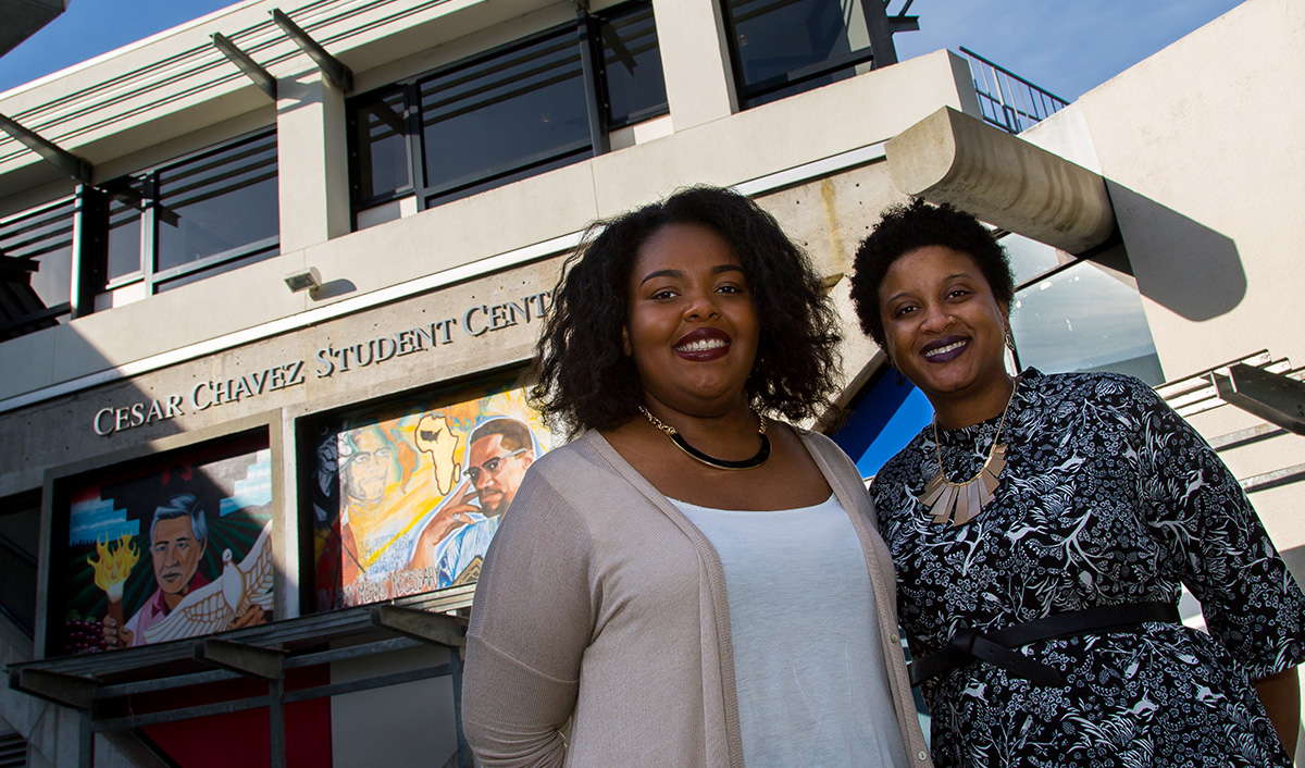 Debate champions Aliyah Shaheed and Genelle Murray are photographed in front of the Malcolm X mural on the Cesar Chavez Student Center
