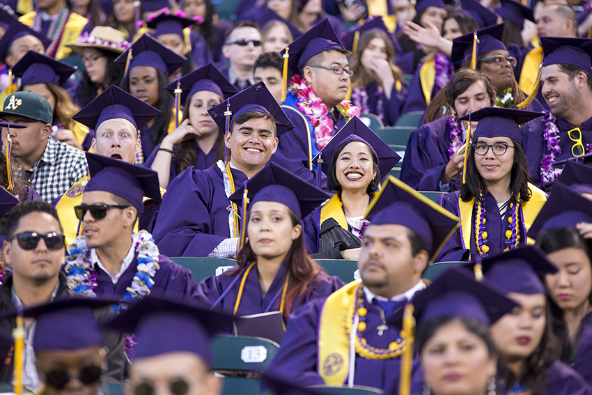 Smiling SF State graduates in their purple robes and mortarboards are in the stands at AT&T Park