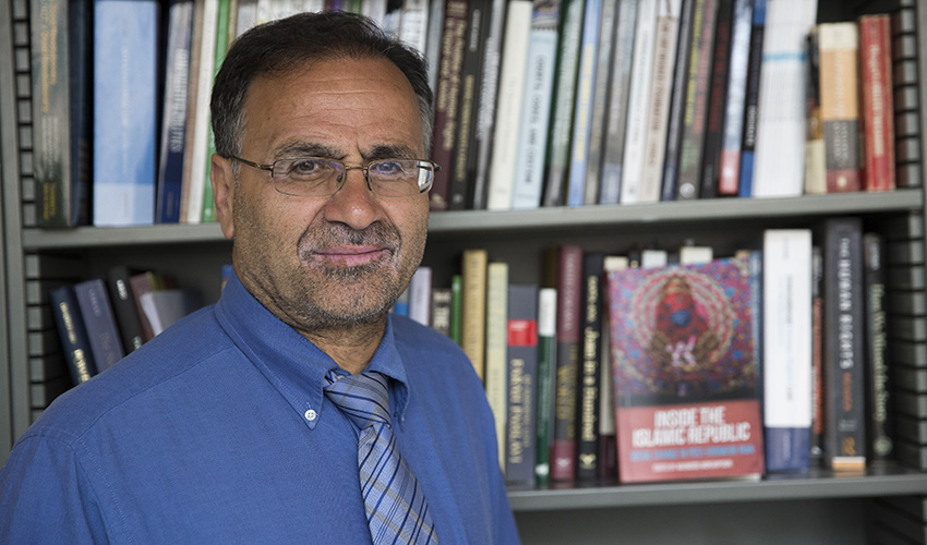 Professor stands in front of book shelf next to his book