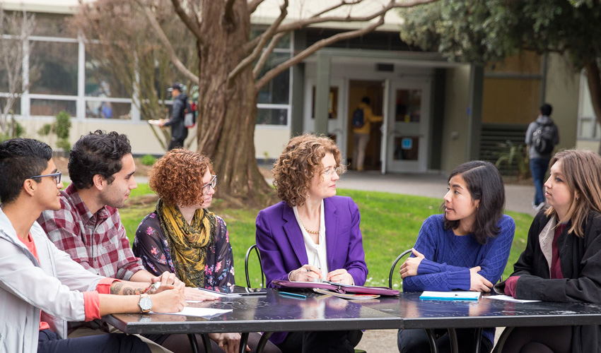 Jennifer Summit, dean of the Division of Undergraduate Education and Academic Planning, is seated at a rectangular table outdoors, flanked by five students.