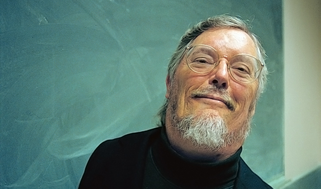 A smiling, bespectacled Paul K. Longmore in front of a green chalkboard