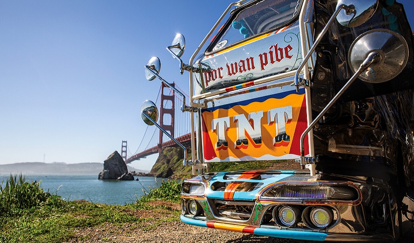 A colorful motorized tricycle with "TNT" written across the front by the Golden Gate Bridge
