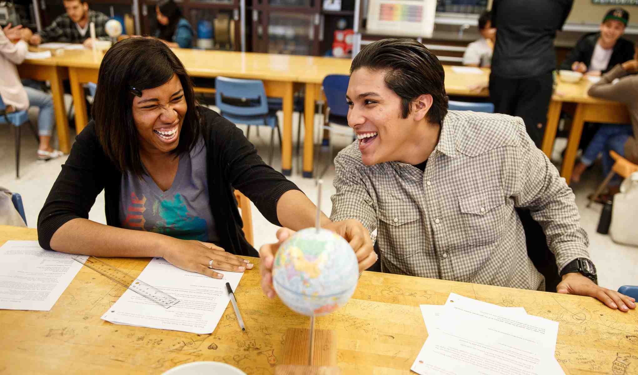 Two students at SF State are laughing and looking at a globe of the world in a classroom.