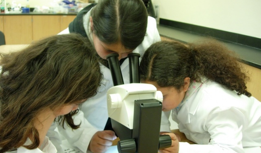 Three middle-school students look into a microscope