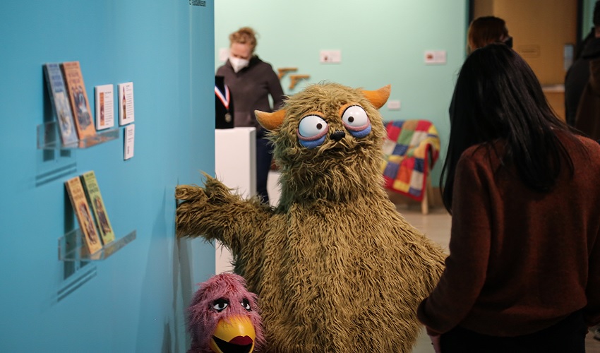 A green puppet welcomes a visitor to a museum exhibit