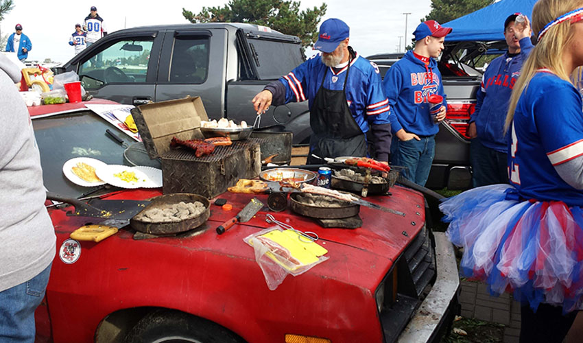 A group of Buffalo Bills fans cooks on the surface of an old Ford Pinto.