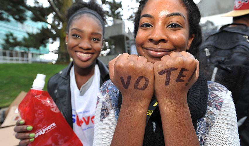 Smiling SF State students, one with "VOTE" written on her hands