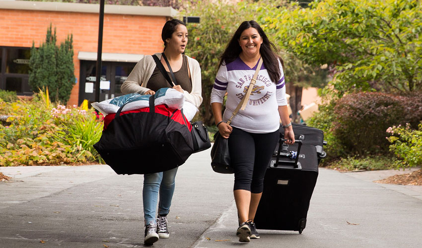 Two new SF State students carry luggage across campus toward the residence halls.