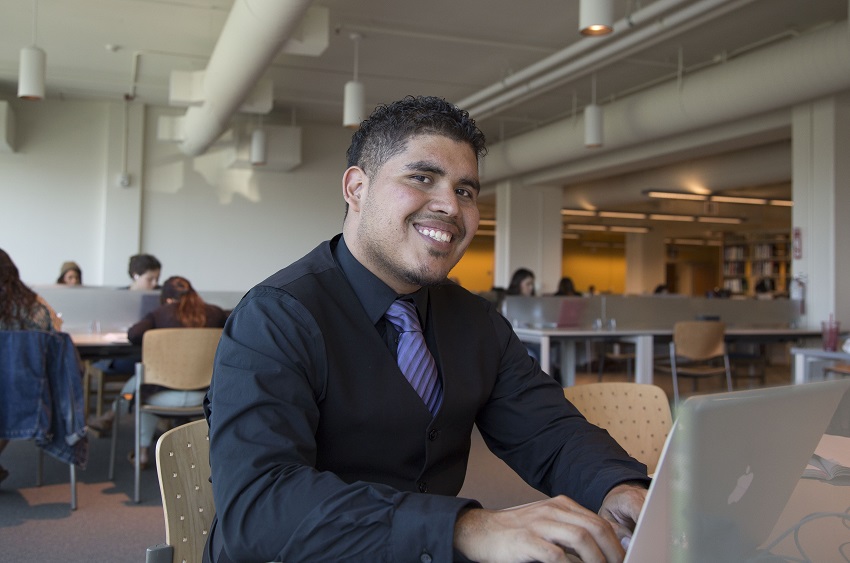 An SF State student smiles as he works on his laptop