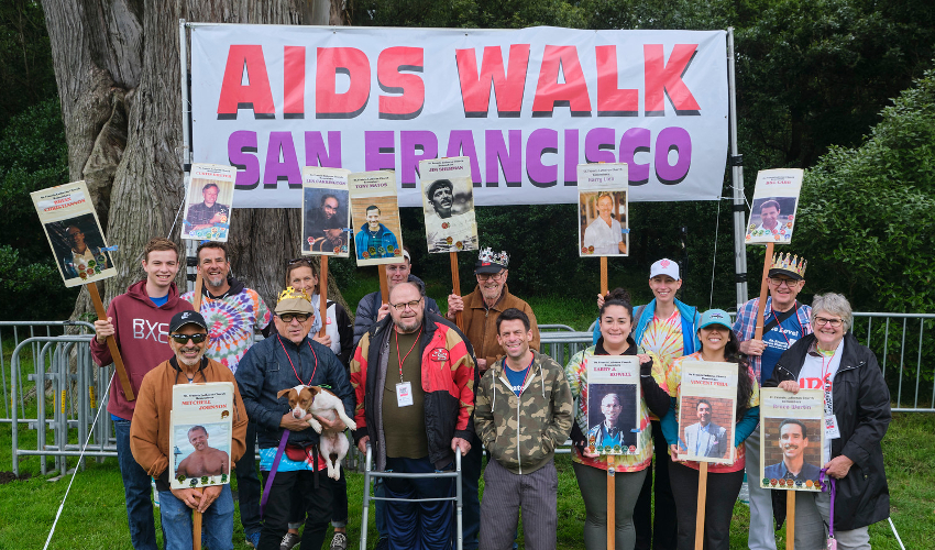 Fourteen people holding signs in front of a banner reading “AIDS WALK San Francisco”