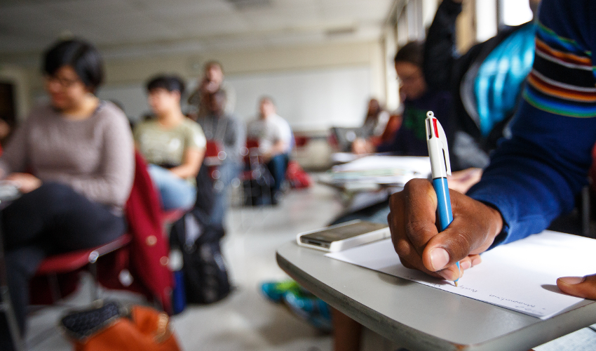 Classroom image with student’s hand taking notes