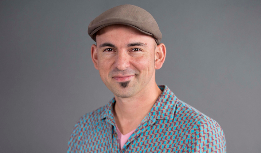Federico Ardila, wearing a cap and a geometric-patterned shirt with, smiles at the camera