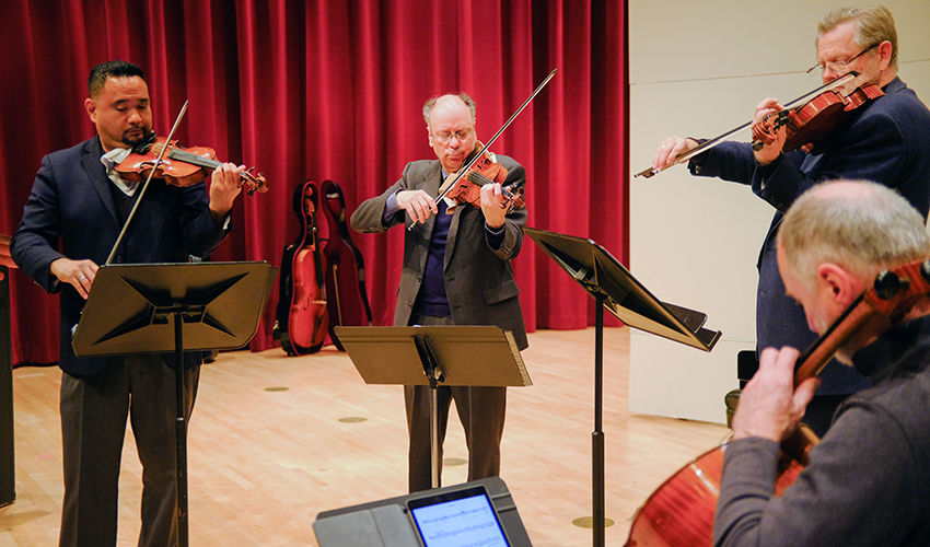Four people standing, playing in a string quartet