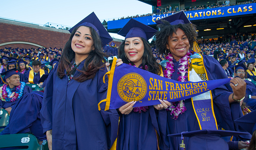 Three graduates holds a SF State pennant at Comemncement