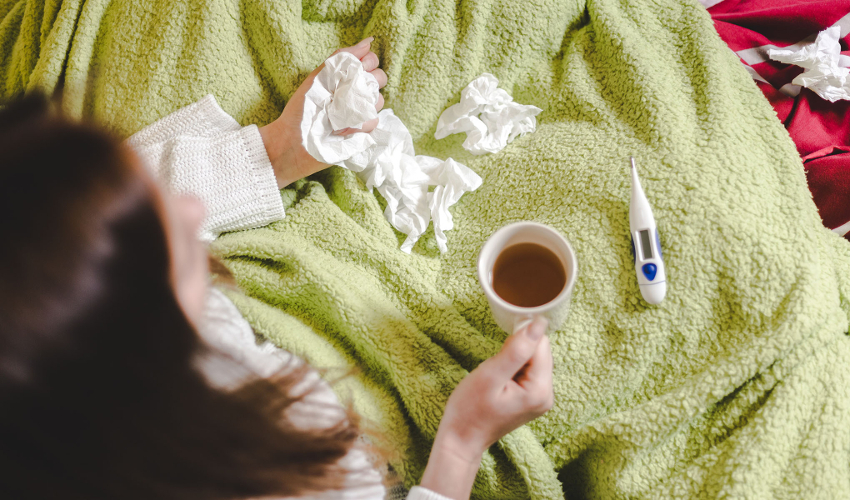 Woman in blanket with tissues, mug of tea and thermometer