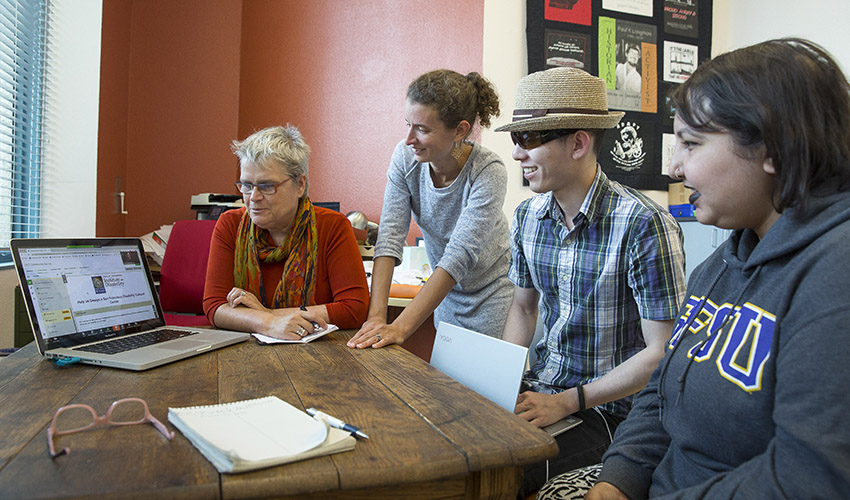 Four members of the SF State planning team sit at a table and view a laptop screen