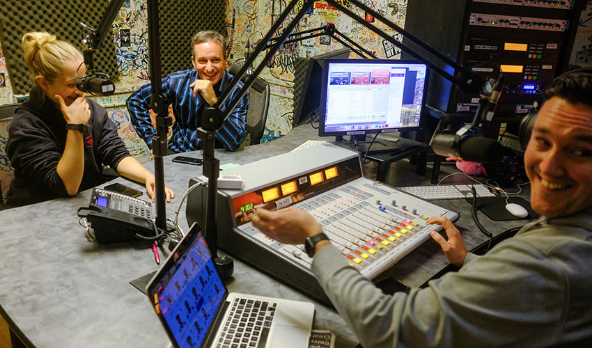 A student and Dennis O'Donnell speak into microphones in a sound booth at SF State