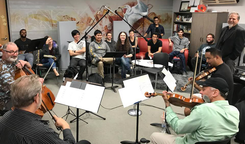 String musicians play their instruments as students watch in a music studio.