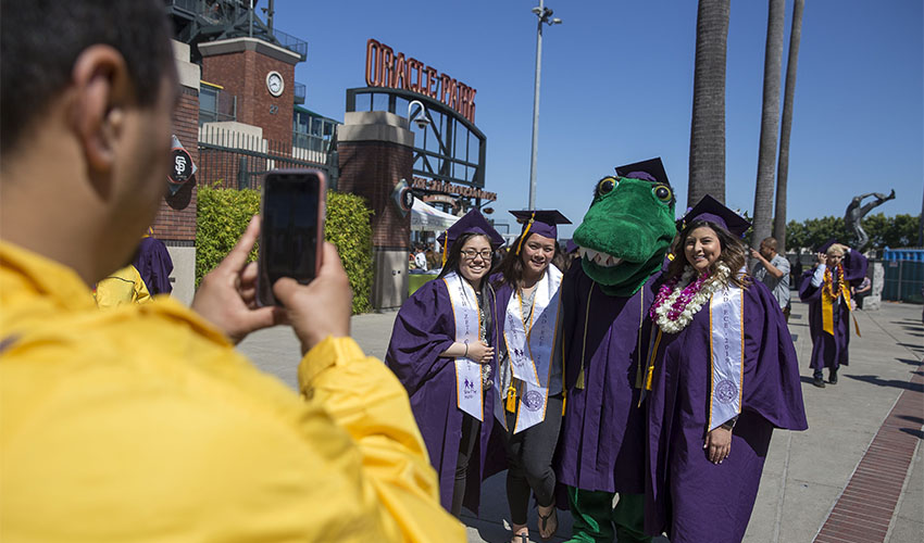 person photographs graduates posing with the Gator mascot in front of Oracle Park