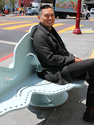 Michael Arcega sitting on a bench smiling