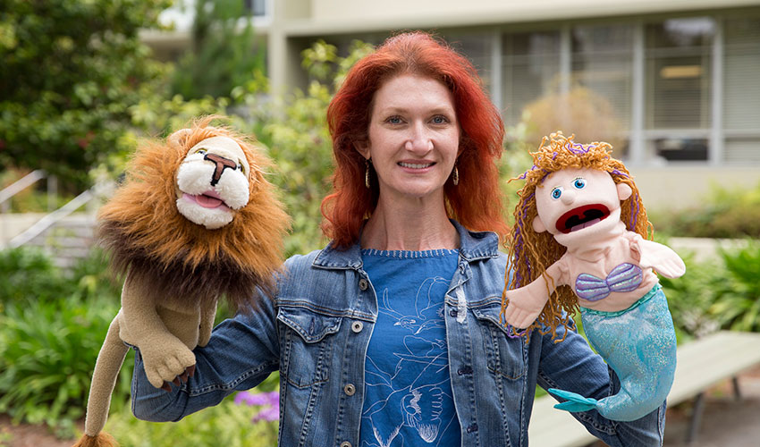 Jenny Debevec holds a lion puppet and a mermaid puppet on her hands to demonstrate one of her improv techniques.