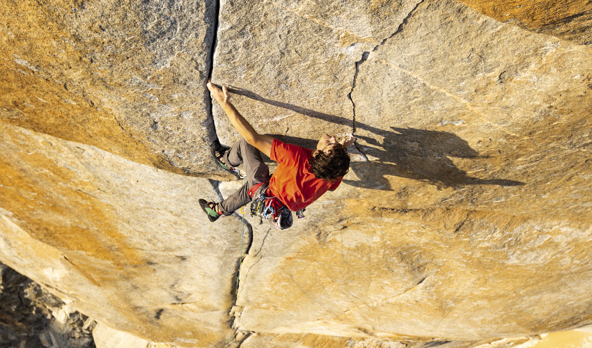 Man in red shirt climbing a granite wall far off the ground