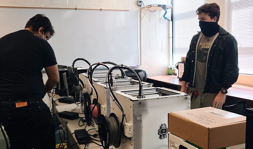 Two people surrounding a table with 3D printers.