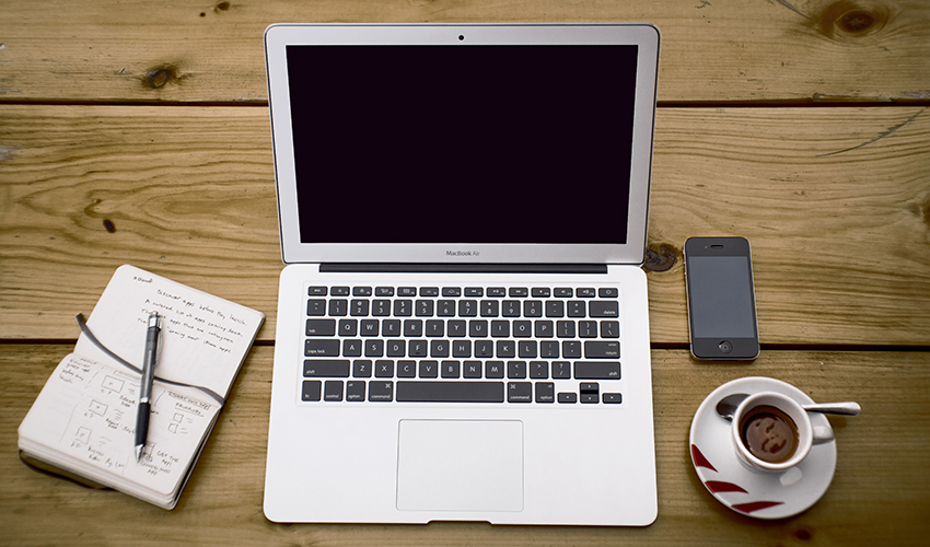 Overhead view of a laptop, a pen on a notebook, phone and a coffee cup on a plate.