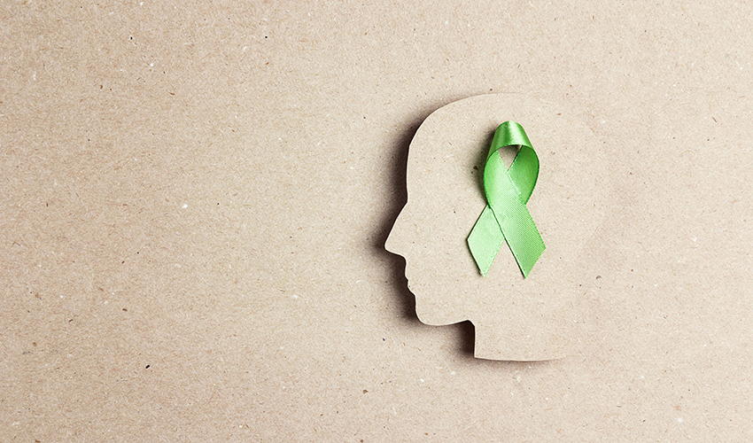 Overhead view of a green ribbon placed on top of a paper cutout of a head shape.
