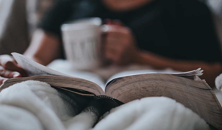 Person reading a book while holding a cup