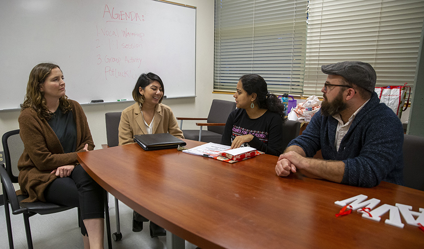 Four people sitting around a wooden table. It appears they are engaging in a conversation.