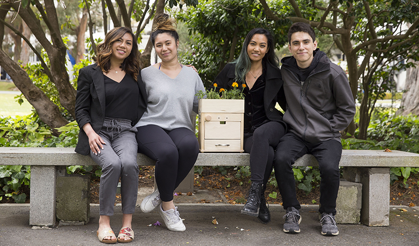 Three female students and one male student posing with their compost machine