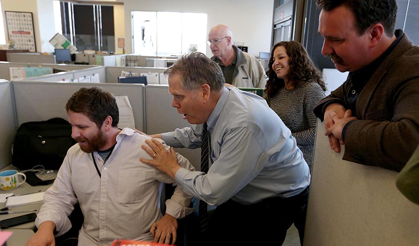 People in a newsroom stand around a computer