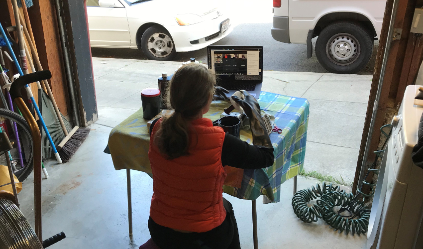 Woman in garage handles film canister, facing a laptop with a videoconferencing program open