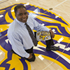 Athletic Director Charles Guthrie, with an SF State Gators shirt, kneeling on the gym center court logo
