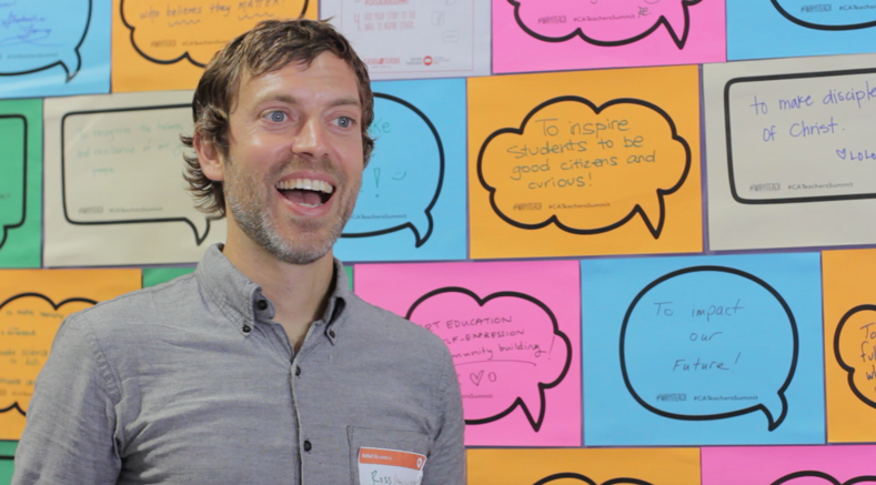 A photo of San Francisco teacher Ross Lefebvre standing in front of a poster where teachers wrote down the reasons why they teach.