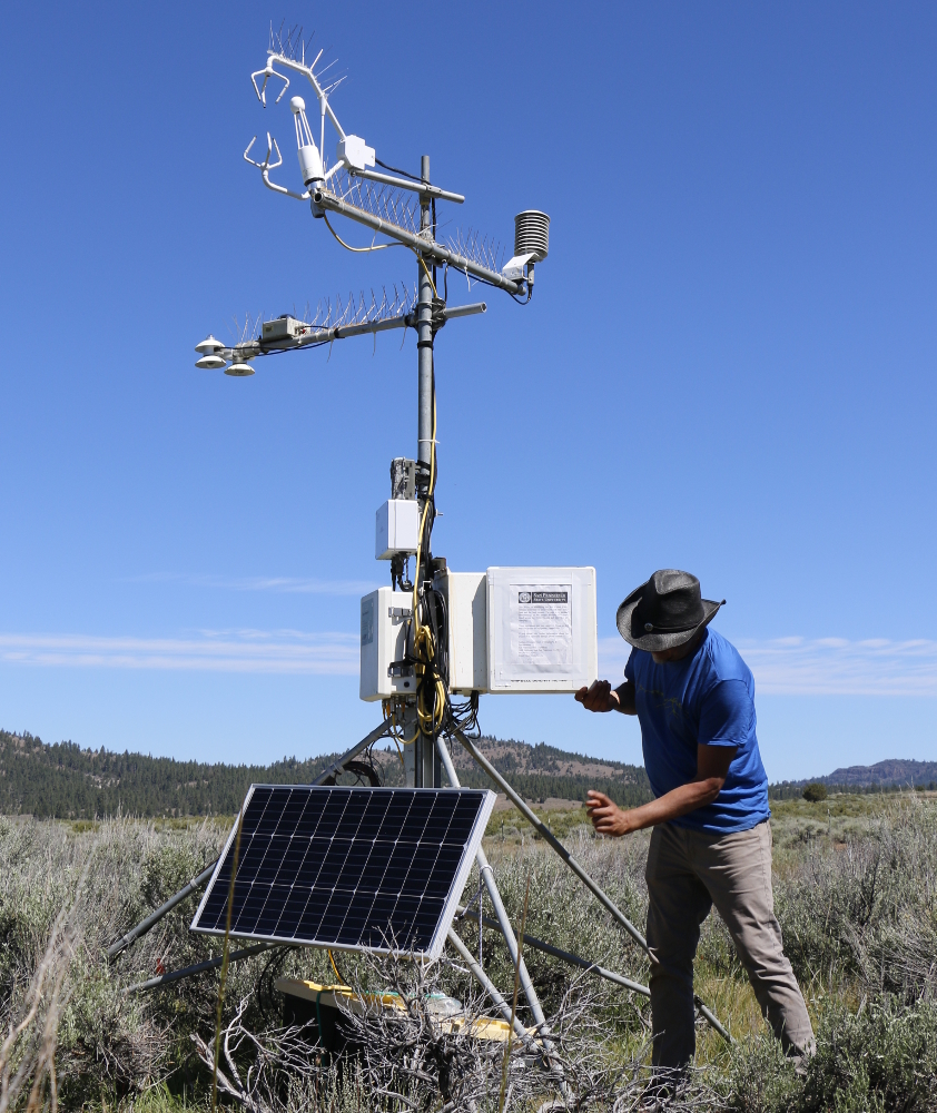 Man in blue shirt and hat adjusts a 10-foot tall instrument on metal poles