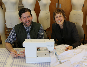 Russell Esmus and Connie Ulasewicz sit behind a sewing machine with a tablecloth
