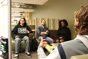 Estevan Lopez points to a whiteboard while Louay Mardini and Bria Grant listen to Emmanuel Lemire during a brainstorming session on couches at the library.