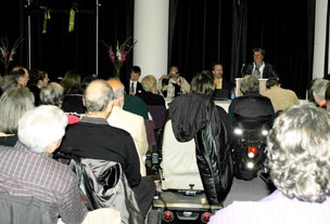 Photo of Catherine Kudlick at a lectern, addressing a crowded audience.