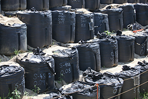 A photo of bags of contaminated soil lined up next to and on top of each other.