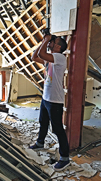 A photo of SF State student Gavin McIntyre taking photos in a destroyed middle school gymnasium.