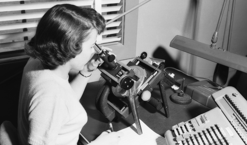 Black-and-white historical photo of woman looking into microscope